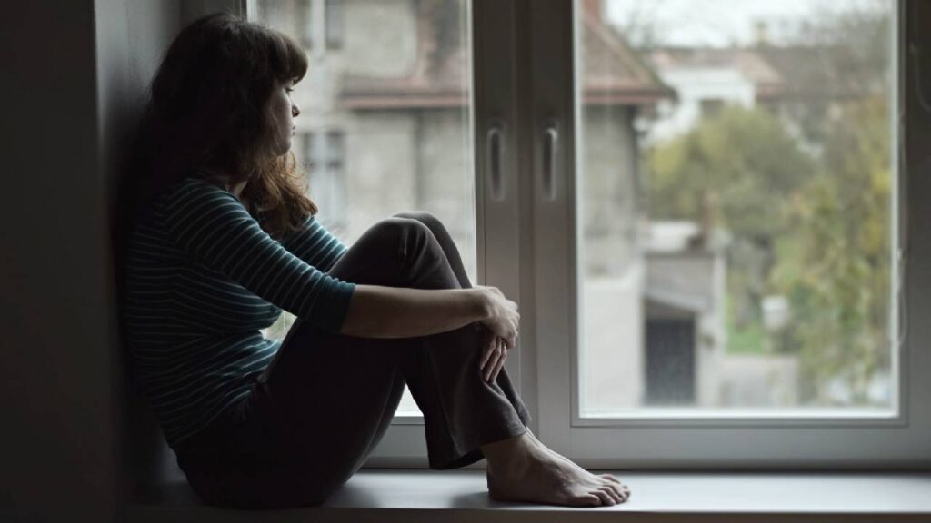 Sad young woman sitting on the window