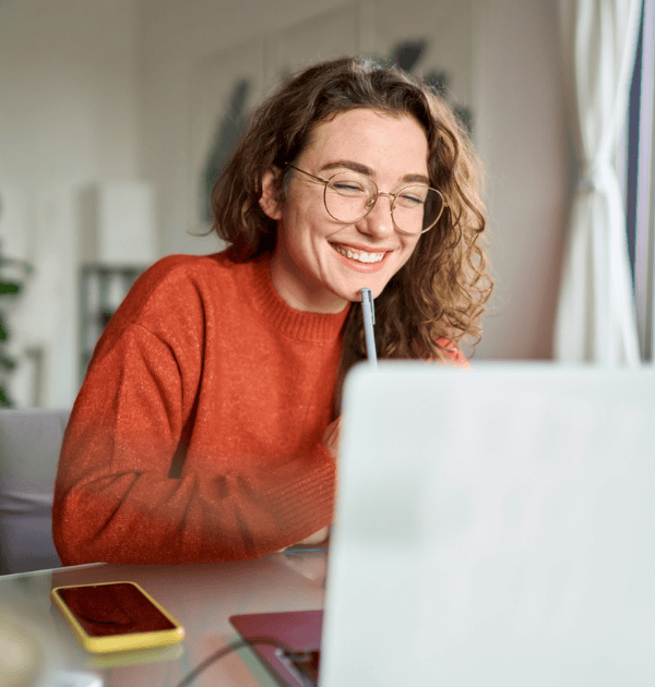 Young happy woman student using laptop watching webinar writing at home.