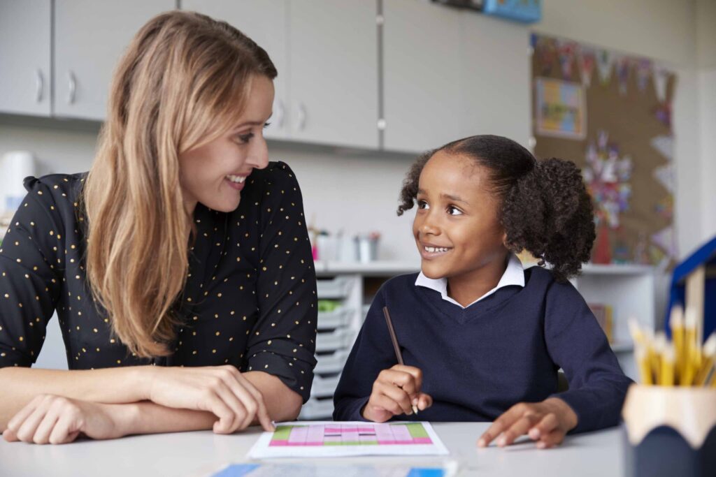Blonde white teaching assistant talking to young black female student. This educator undertook our Advanced Safeguarding, Child Protection and Prevent