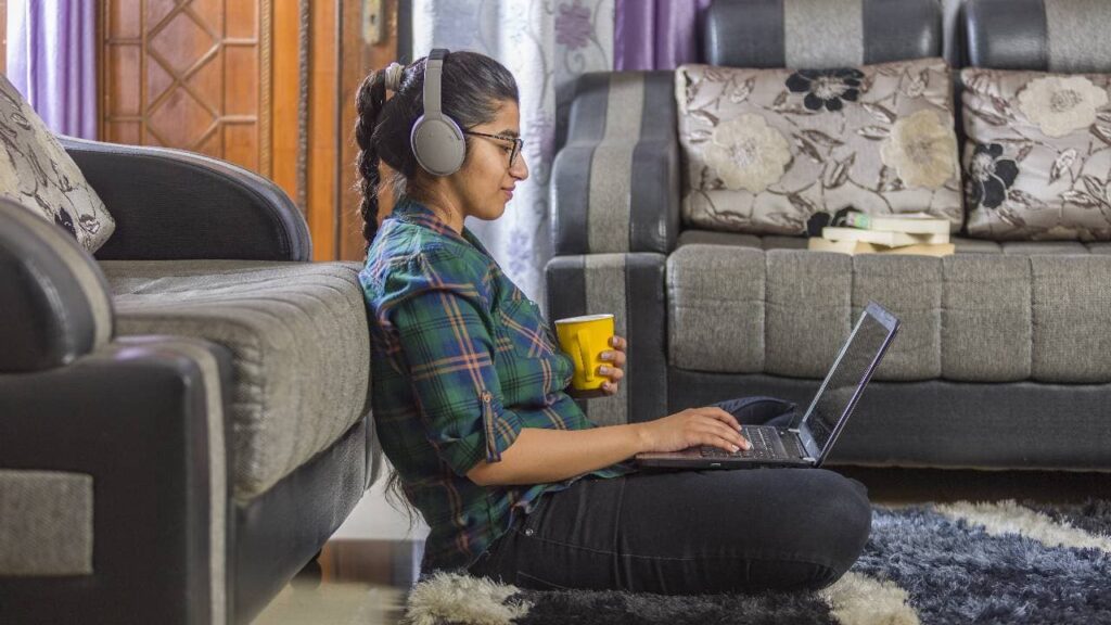 An Indian female teacher using laptop, sitting on floor at home.