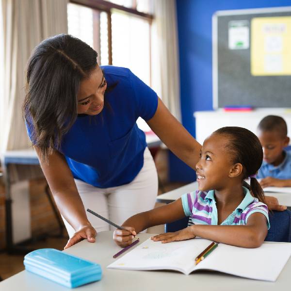 African american female teacher teaching african american girl in the class at elementary school